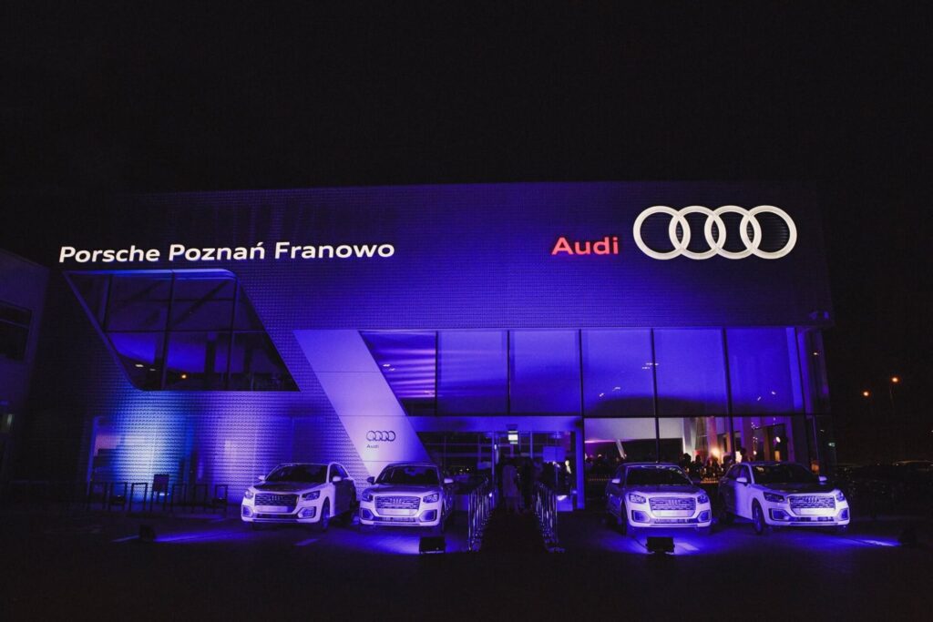 Salon samochodowy noca w niebieskim oswietleniu, samochody przed budynkiem