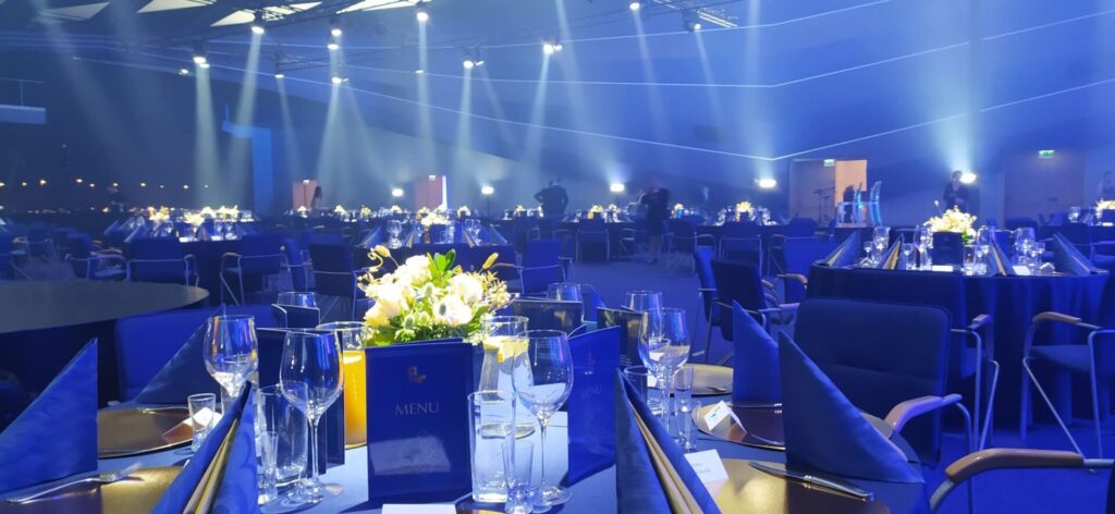 Sala bankietowa w niebieskim oswietleniu, stoly z granatowymi serwetkami i kartami menu